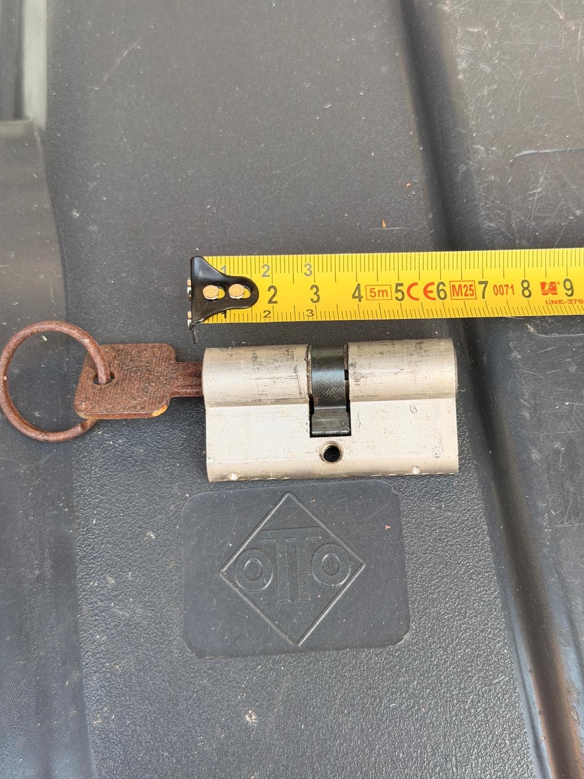 Euro profile lock cylinder with a rusty key inserted, measured by a yellow tape.